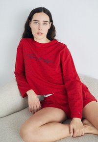 Röd lounge-set bestående av en långärmad topp med marinblåa prickar och logotyp, tillsammans med matchande shorts, mjukt tyg och bekväm passform.