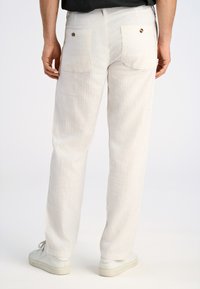 Witte linnen broeken met een ontspannen pasvorm, voorzien van twee achterzakken met ronde kleppen en een zachte, gestructureerde stof. Gekleed met witte sneakers.