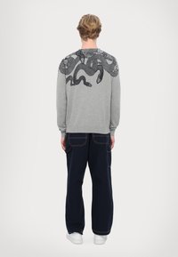 Felpa grigia con grafica di un serpente nero sul retro, con polsini e orlo a costine, abbinata a pantaloni blu navy con tasche e cuciture a contrasto.