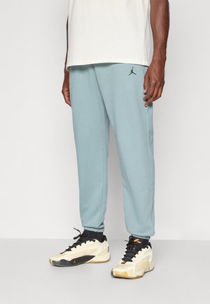 Lyseblå joggerbukser med elastisk talje og tætsiddende ankler, med et sort Jumpman-logo på venstre lår. Bæres med hvide og sorte sneakers.
