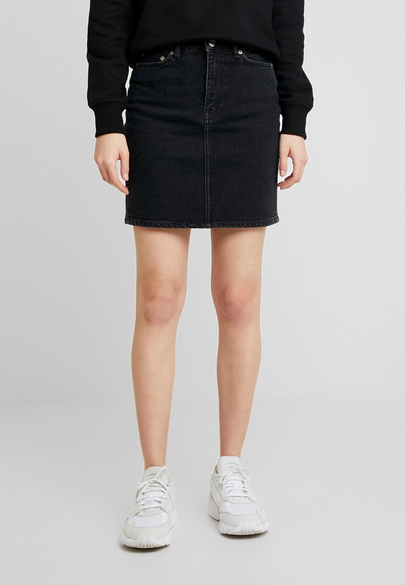 Sort denim nederdel med en tætsiddende silhuet, frontlukning med knapper og fem lommer. Sammen med hvide sneakers for kontrast.