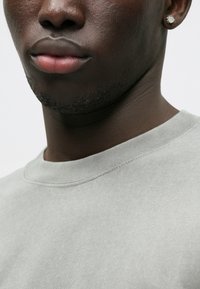 Γκρίζα φούτερ με στρογγυλή λαιμόκοψη, ριγωτή υφή και ορατές ραφές. Κοντινή λήψη χεριών και αυτιών με ένα σκουλαρίκι.