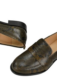 Een paar donkerbruin en zwart leren loafers met slangenhuidstructuur, met lage hakken en pennybandjes op een witte achtergrond.
