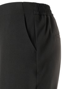 Schwarze Hosen aus glattem Stoff, mit elastischem Bund, seitlichen Taschen und einem schlanken Design. Nahaufnahme der Seitenansicht zeigt die Nahtdetails.