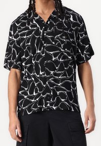 Košile s krátkým rukávem v černé tkanině s odvážným bílým abstraktním vzorem, s klopovým límcem a volným střihem.