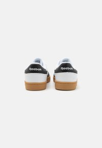 Baltas apavums ar melniem akcentiem, ar zemas augstuma dizainu, teksturētu ādas virsējo daļu un gumijas zoli. Reebok logo uz papēža.