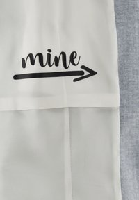 Weißer Stoff mit schwarzem "mine"-Text und Pfeilgrafik. Die Textur ist glatt und zeigt auf der linken Seite ein schlichtes Design, das im Kontrast zu einem grauen Abschnitt steht.