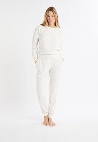 Kremowy zestaw ubrań do noszenia w domu, składający się z bluzy z pulowerem i zwężanych spodni dresowych, wykonany z miękkiego materiału z teksturowanymi wzorami oraz ściągaczami na mankietach.