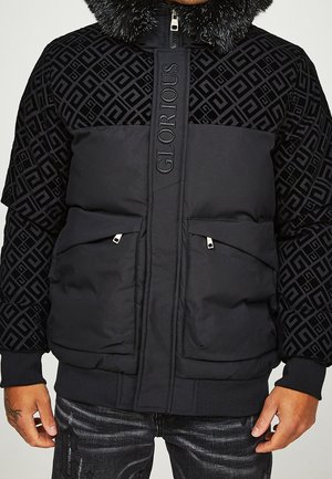 Czarna pikowana kurtka z futrzanym kołnierzem, geometrycznym wzorem na rękawach i ramionach, centralną plisą na zamek błyskawiczny z napisem „GLORIOUS” oraz przednimi kieszeniami na zamek.