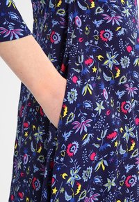 Navy blue fabric with a floral pattern in red, yellow, and blue. Features a pocket and short sleeves, made from a soft, flexible material.