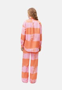 Completo a due pezzi a righe in arancione e rosa. La maglietta ha una vestibilità ampia con polsioli a bottoni; i pantaloni sono a gamba larga e coordinati nel design.