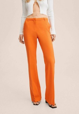 Kvinde iført højtaljede, knækkede, skarpt orange bukser med lige ben, hvid croppet ribstrikket langærmet top og sorte åbne tå-højhælede sandaler.