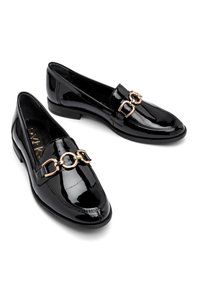 Mustat lakatut loaferit, joissa on pyöristetty kynkä, kultaketju koristeena yläosassa ja matala pinottu korko.