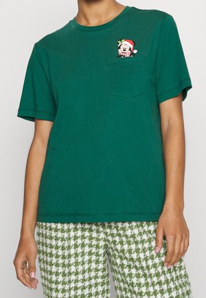 Zielona koszula z krótkim rękawem z małym Myszka Miki w czapce Mikołaja nad lewą kieszenią na piersi, w połączeniu z zielonymi i białymi spodniami w pepitkę.