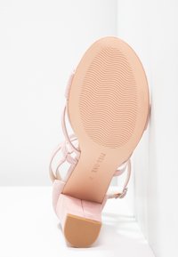 Sandale à talon en daim rose montrée par la semelle avec un motif ondulé et une sangle à boucle, taille 37 estampillée sur la semelle.