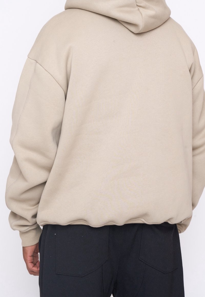 Felpa con cappuccio beige a vestibilità rilassata, caratterizzata da una tasca a marsupio e polsini a costine, abbinata a pantaloni neri. Tessuto dal tocco morbido.