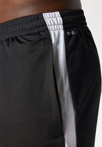 Svart trening Shorts med en jevn tekstur, har en hvit stripe på siden og elastisk midje. Subtil merkevare synlig.