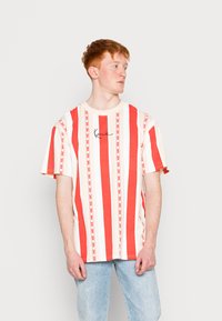 Rød og hvid stribet t-shirt med korte ærmer, der har et minimalistisk design og broderet branding på brystet.