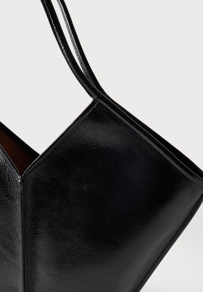 Μαύρη γυαλιστερή δερμάτινη τσάντα χειρός με δύο λεπτές λαβές, που δείχνει λεπτομερή υφή και ραφές σε ένα απλό ανοιχτό φόντο.