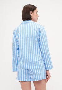 Lichtblauw en wit gestreept pyjama set van katoen, met een knoopsluiting lange mouwen shirt en bijpassende shorts. Subtiele logo patroon.