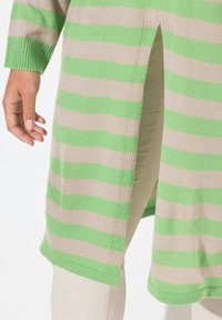 Tunic a maglia a righe con strisce orizzontali verdi e beige, fessure laterali e un design testurizzato. Mano visibile vicino all'orlo.