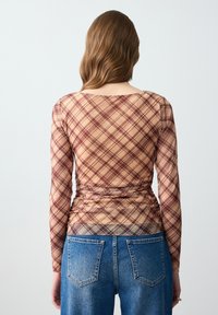 Langarmtop met een aansluitende pasvorm, met een tan- en bordeauxruitpatroon. Gecombineerd met hooglopende blauwe denim jeans.