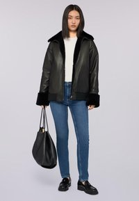 Chaqueta de cuero negra con un cuello de pelaje sintético, cierre de cremallera y puños acanalados, combinada con jeans azules y un bolso negro de hombro.