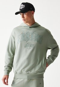 Ανοιχτό πράσινο φούτερ με κουκούλα και ανάγλυφο σχέδιο των Los Angeles Lakers. Διαθέτει εφαρμοστή μέση και κουκούλα. Μαύρο καπέλο με το λογότυπο των Lakers.