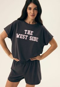 Dark gray casual outfit featuring a loose-fitting T-shirt with "THE WEST SIDE" in bold pink lettering and matching elastic waist shorts.
