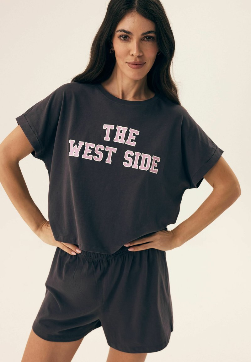 Dark gray casual outfit featuring a loose-fitting T-shirt with "THE WEST SIDE" in bold pink lettering and matching elastic waist shorts.
