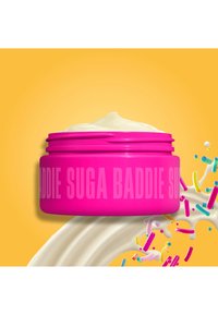 Felroze potje crème met tekst "SUGA BADDIE", romige draaikolk eronder en kleurrijke sprinkels op een gele achtergrond.
