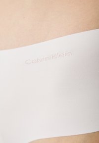 Calvin Klein bijeli bešavni bandeau top izrađen od mekog materijala, s glatkom teksturom i suptilnim brendiranjem u svijetloj nijansi.