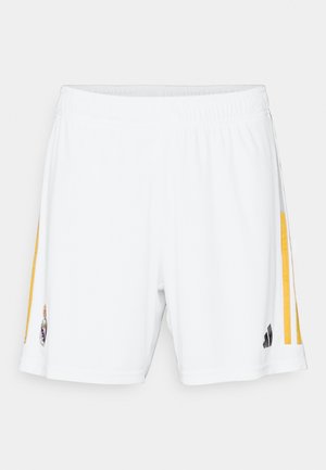 Pantalones cortos de fútbol blancos con franjas laterales amarillas, cintura elástica y acentos en negro. Presenta un logo con detalles ornamentales en la parte inferior izquierda.