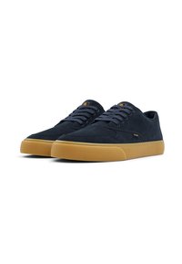 Zapatillas de ante azul marino con un perfil bajo, que presentan una puntera redonda, suela de goma beige y cordones grises. Detalle del logo amarillo en la lengüeta.