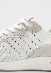 Białe i jasnoszare sneakersy wykonane z zamszu i materiałów tekstylnych, z akcentami z kryształków, sznurowanym zapięciem oraz teksturowaną podeszwą.