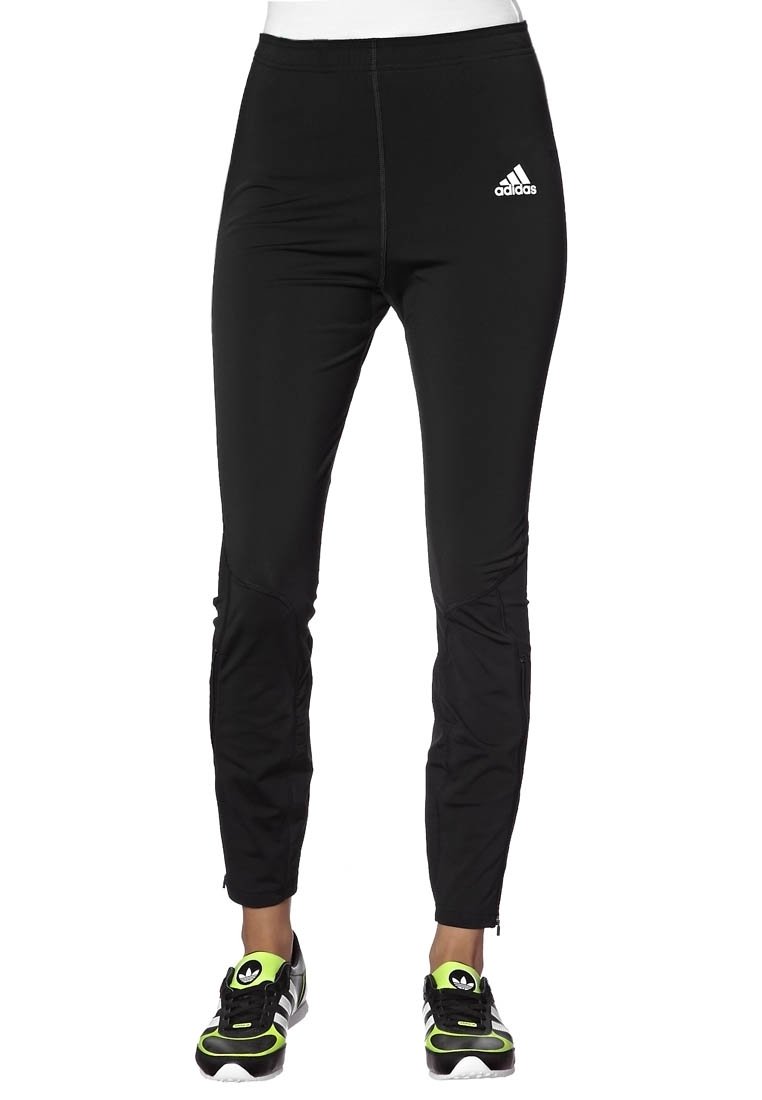 Czarne legginsy sportowe o dopasowanym kroju, gładkiej fakturze oraz białym logo Adidas na lewym udzie. Zapięcia na suwak przy kostkach.