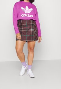 Lila sweatshirt med vit Adidas-logga, rutiga kjolen i brunt, grönt och rosa, som bärs med vita sneakers och lavendelfärgade texturerade strumpor.