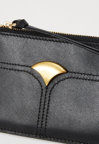 Black leather wallet with a textured surface, featuring a prominent curved gold accent and a contrasting zip closure with golden hardware.