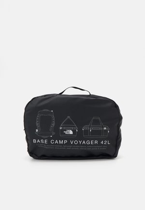Zwarte reistas met handvat, met omlijnde diagrammen van rugzak-, duffel- en draagstijlen, vooraan gelabeld met "Base Camp Voyager 42L".