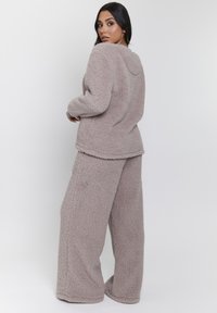 Conjunto de loungewear de felpa en suave taupe, que incluye un pullover holgado con capucha y pantalones de pierna ancha, ambos texturizados y acogedores.