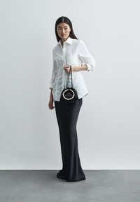 Λευκό πουκάμισο με μακριά μανίκια και ζαρωτή υφή, συνδυασμένο με μια εφαρμοστή μαύρη φούστα. Κρατάει μια μικρή μαύρη τσάντα με λαβή διακοσμημένη με πέρλες.