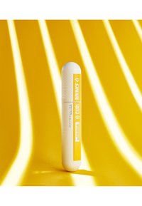 Mascara Maybelline avec un tube blanc texturé et une étiquette jaune. Forme lisse avec un bout arrondi. L'arrière-plan pr�ésente des rayures jaunes.