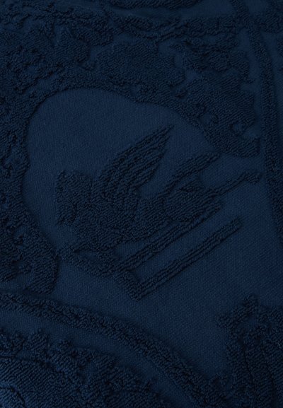 Gros plan détaillé d'un tissu bleu foncé avec un motif gaufré texturé représentant un oiseau aux ailes déployées.
