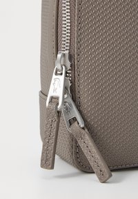 Texturerat grå ryggsäcksmaterial med silverfärgade dragkedjor och läderdragningar. Dragkedjedetaljerna förbättrar designens funktionalitet och stil.