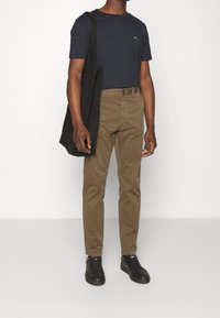 Kaki byxor och en marinblå t-shirt, båda välsittande. T-shirten har en liten logotyp; outfiten är kombinerad med en svart tote och svarta sneakers.