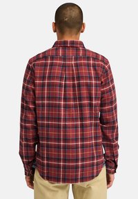 Camicia in flanella a quadri rossi e neri con maniche lunghe, orlo dritto e polsini con bottone. Presenta una texture morbida ed un design con colletto classico.
