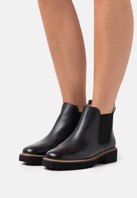 Černé kotníkové kožené boty s elastickými bočními panely, plochou gumovou podrážkou a kulatou špičkou. Texturovaný povrch a jemné šití.