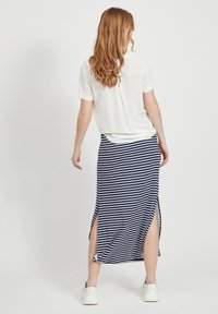 Jupe maxi rayée bleu marine et blanc avec de grandes fentes latérales, associée à un haut blanc uni à manches courtes et des baskets blanches. Tissu doux et extensible.