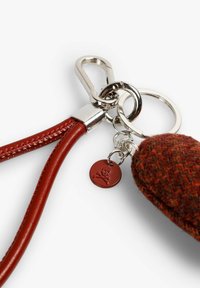 Llavero de cuero rojo con un clip y anillo de plata, que presenta un elemento texturizado de lana y un pequeño charm rojo con un logotipo de calavera en relieve.
