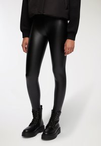 Leggings in finta pelle nera con una finitura liscia e lucida. Abbinati a stivali combat neri con lacci, caratterizzati da suole spesse e occhielli metallici.